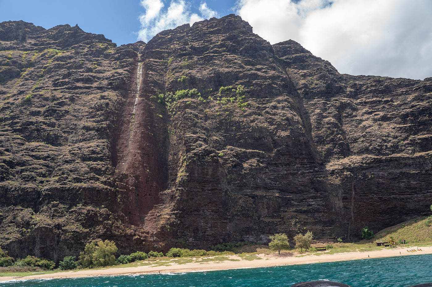 waterfall-scar-na-pali-coast.jpg Thin waterfall tracing a red channel down a Na Pali cliff above the beach