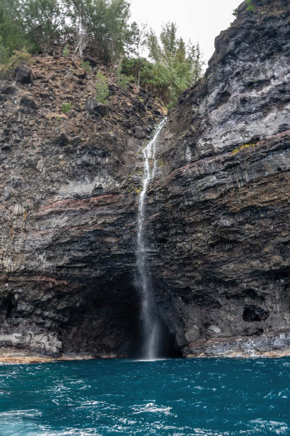 na-pali-coast-cave-waterfall.jpg Waterfall dropping from layered sea cliffs into the ocean