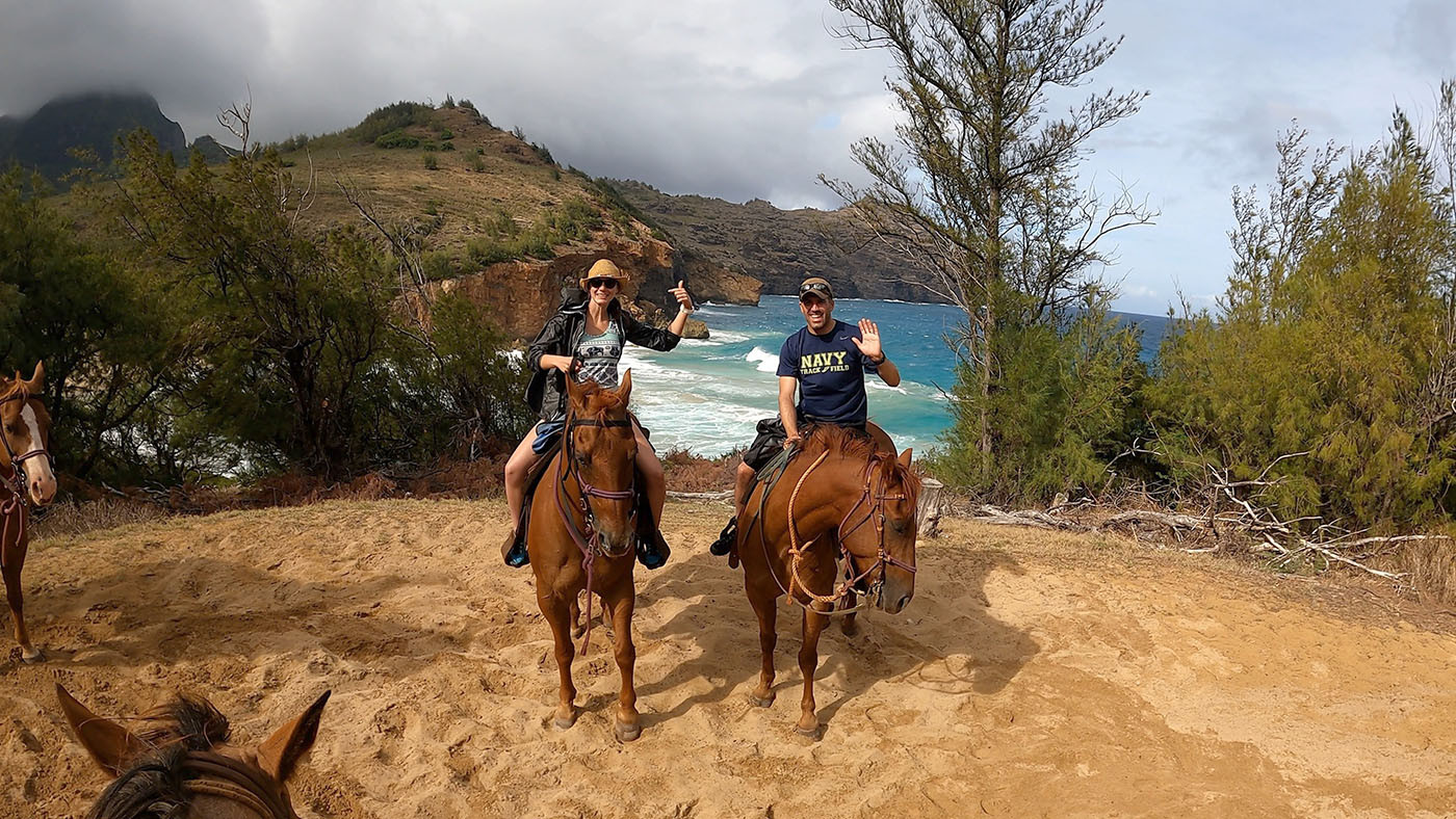 horseback-riding-date-kauai.jpg Couple waving from horseback at a coastal overlook on Kauai