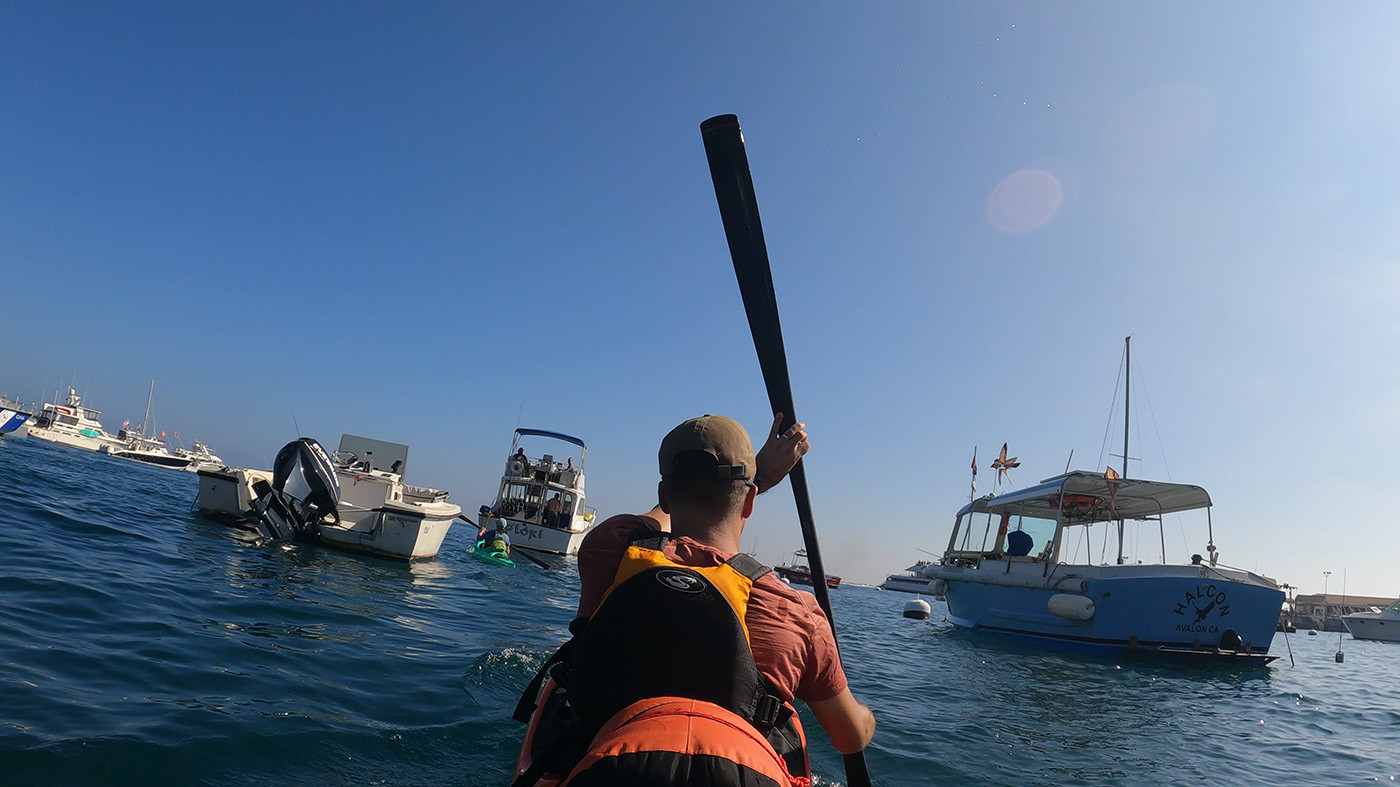 Kayaker paddling an orange Pakayak through boats in Avalon Harbor