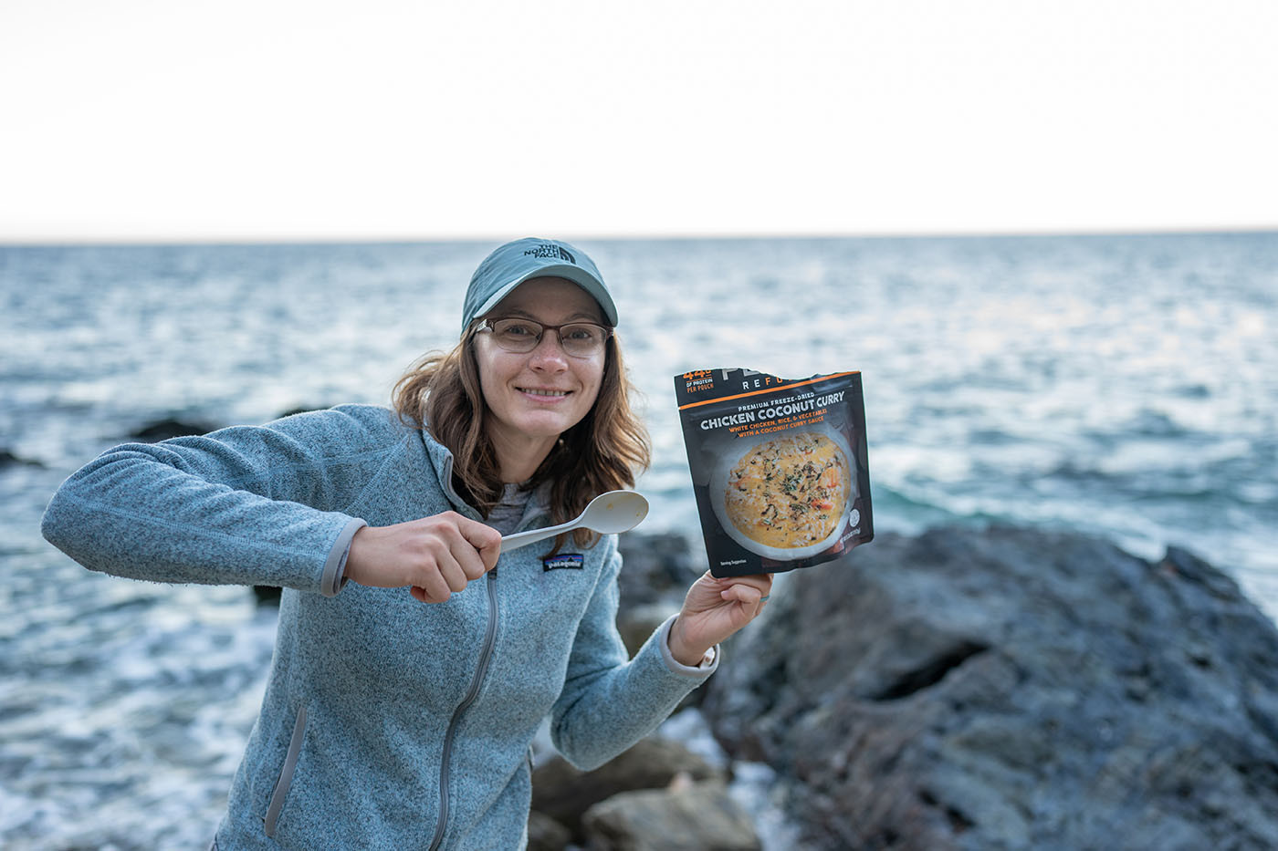 Camper holding a chicken coconut curry meal beside the ocean