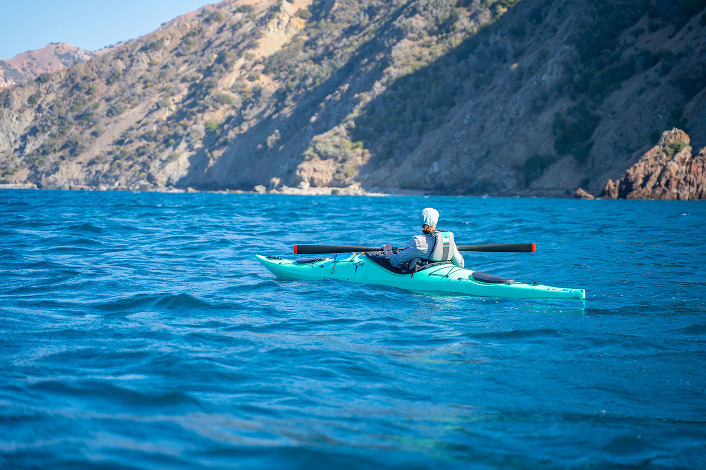 Kayaker resting in a teal Pakayak against the rugged Catalina coast