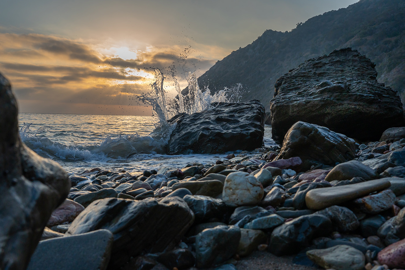 Wave splashing over dark shoreline rocks at sunrise on Catalina Island