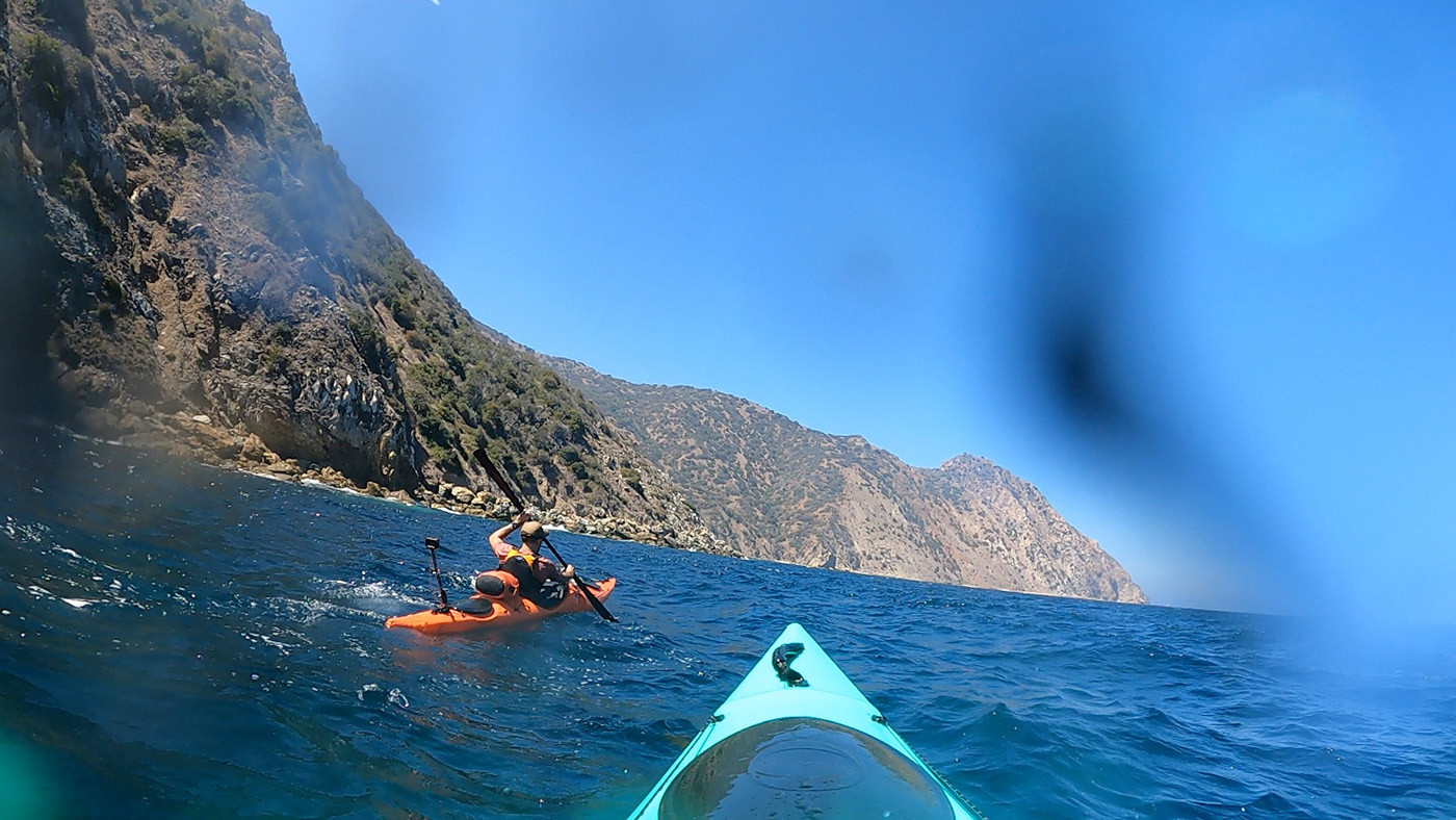 Orange and teal kayaks crossing choppy water near Long Point cliffs