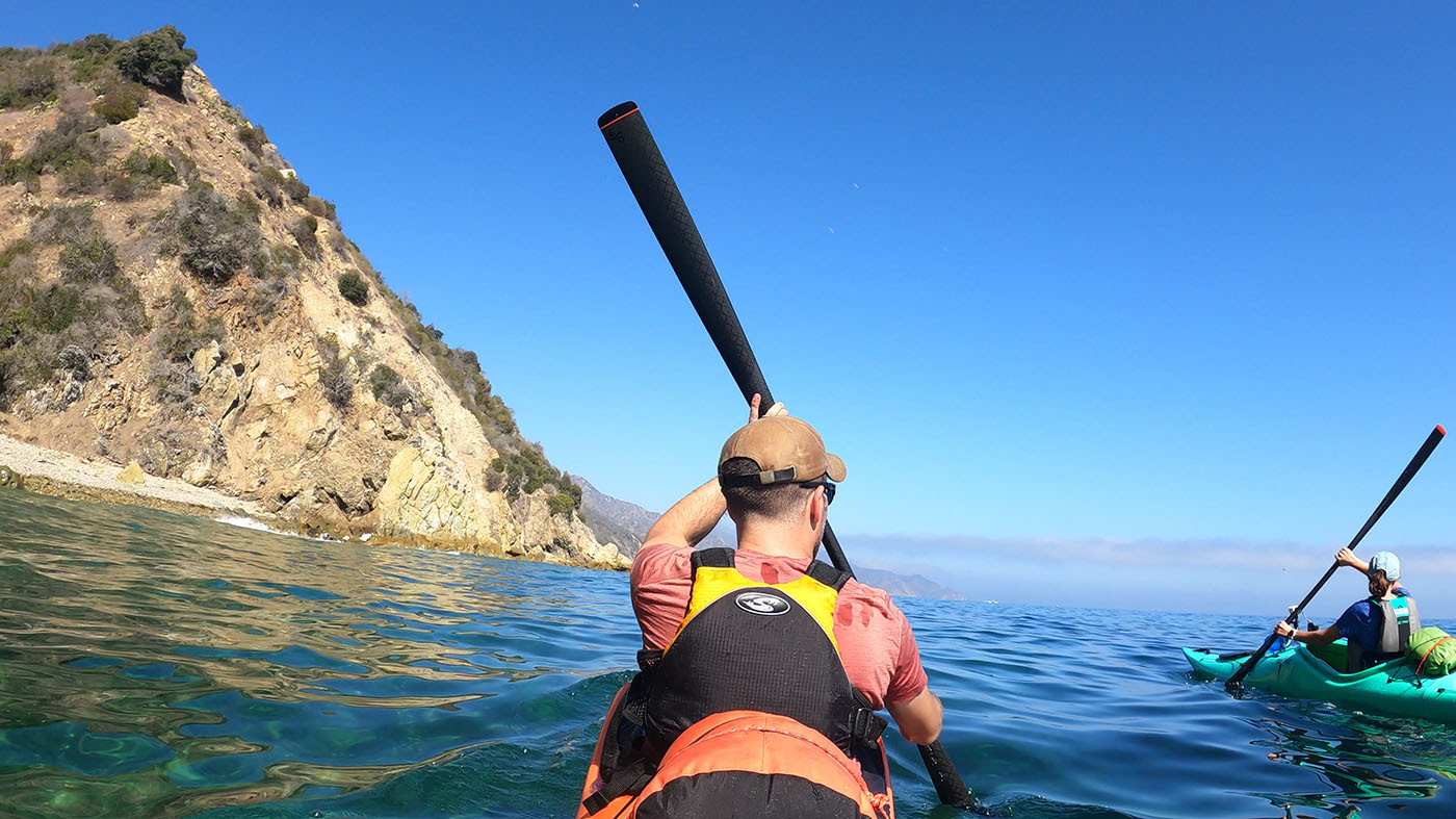 Two kayakers paddling calm blue water beneath Catalina Island cliffs