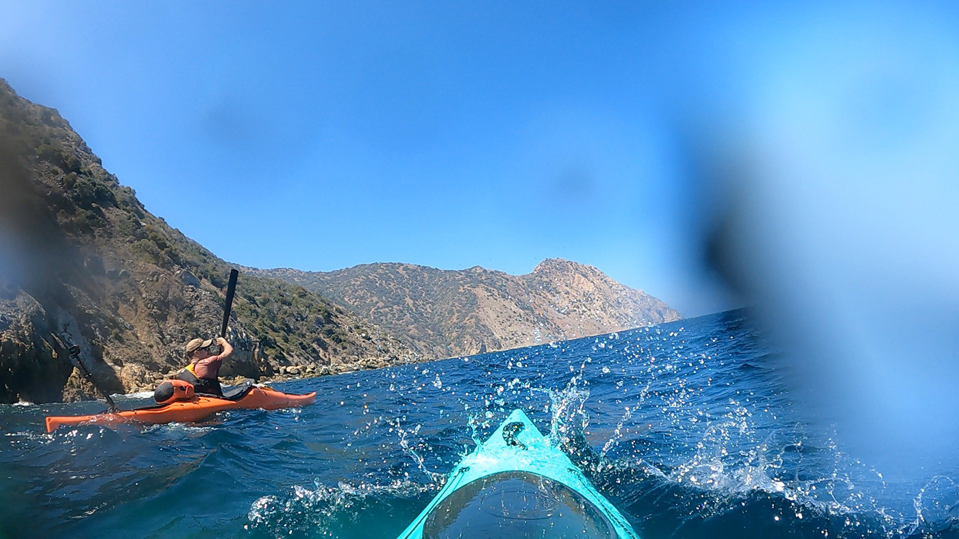 Sea spray breaking over a teal kayak beside an orange kayak near Long Point