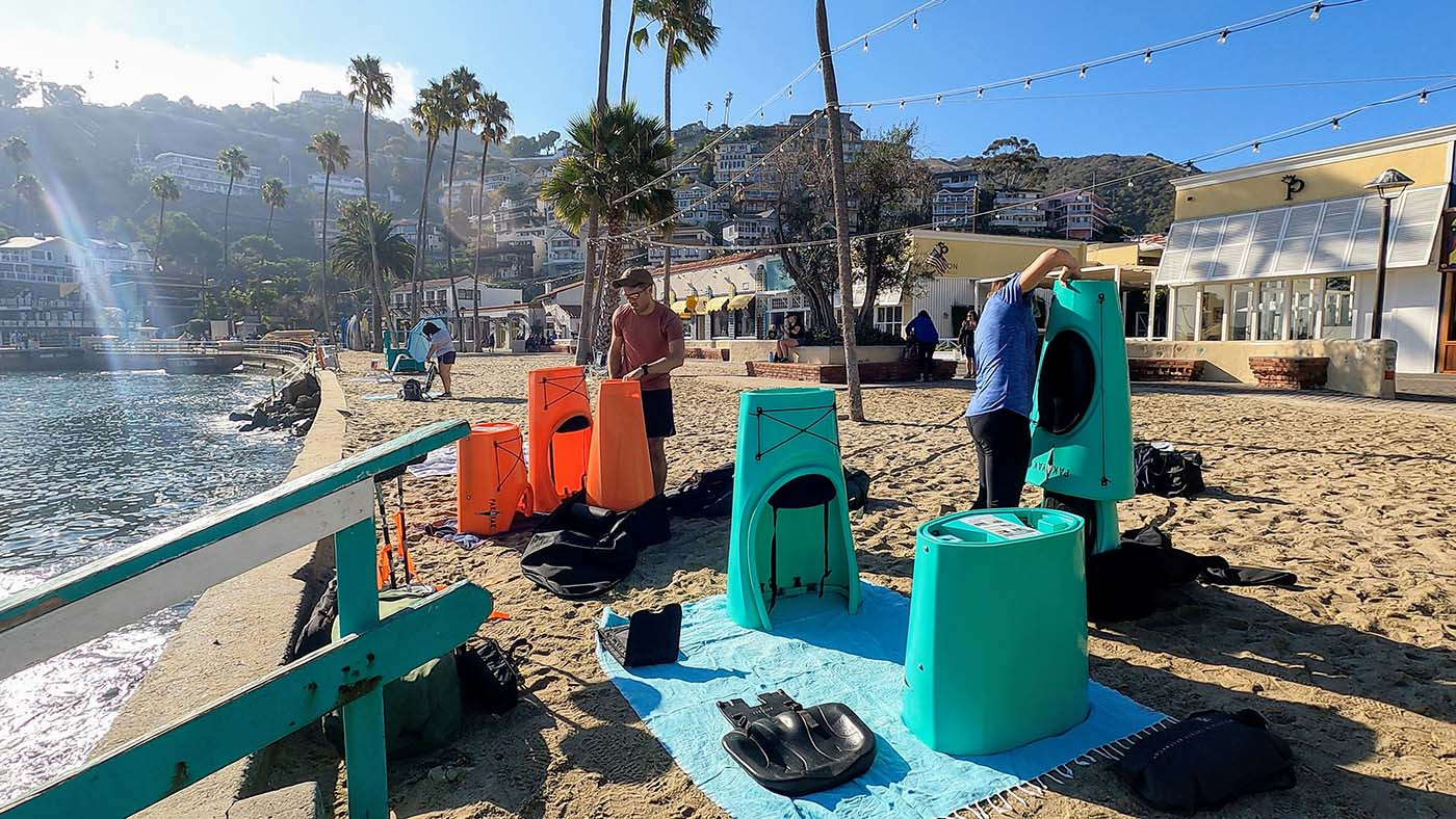 Two kayakers assembling orange and teal Pakayaks on an Avalon beach